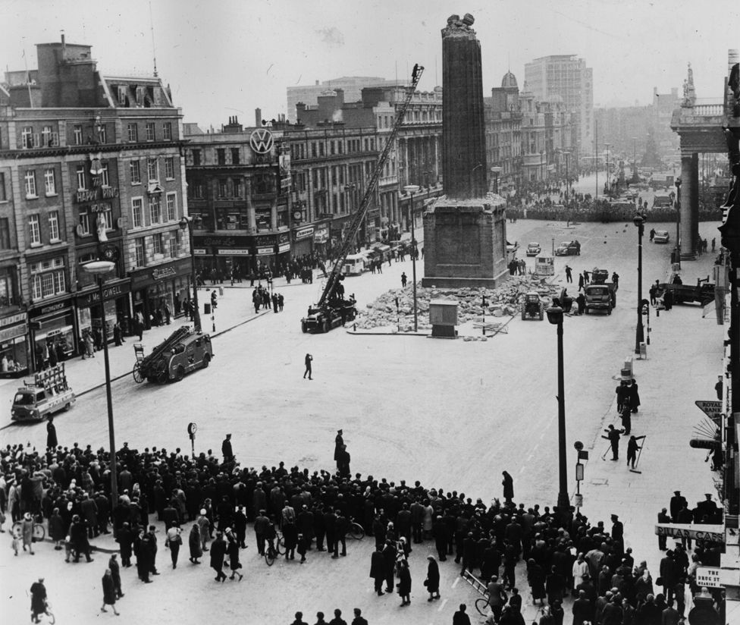 Image depicting the ruin of Nelson's Column in Dublin with a large crowd standing some way back.
